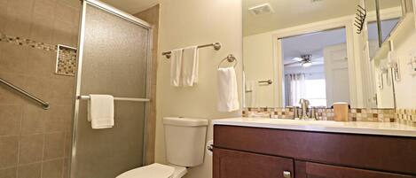 A bathroom with a glass shower enclosure, a toilet, a vanity with a mirror, and a towel rack.