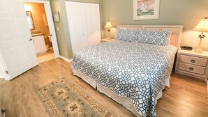 Un dormitorio con cama, mesitas de noche, un tapete y una puerta que da a otra habitación.