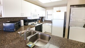 Una cocina compacta con armarios blancos, microondas, estufa, lavaplatos y lavadora y secadora integradas.