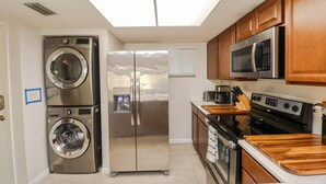 A compact kitchen with a stainless steel washer, refrigerator, microwave, stove, and wooden cabinets. - Ocean Village Club Condo G22 (St. Augustine)
