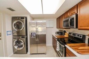 A compact kitchen with a stainless steel washer, refrigerator, microwave, stove, and wooden cabinets.