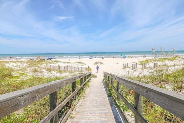 A wooden boardwalk leading to a sandy beach with a clear sky.