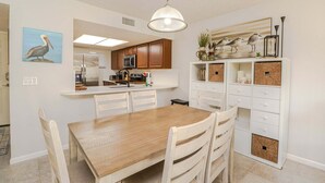 A dining area with a wooden table and chairs, a kitchen with wooden cabinets and a refrigerator, and a hanging light fixture. - Ocean Village Club Condo G22 (St. Augustine)