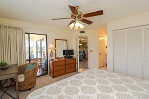 A bedroom with a bed, a dresser, a television, a ceiling fan, and a view of the outside. - Ocean Village Club Condo H21 (St. Augustine)