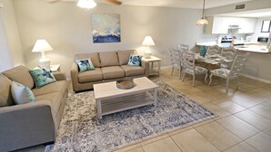 A living room with a sofa, coffee table, and dining area with chairs and a table. - Ocean Village Club Condo J16 (St. Augustine)