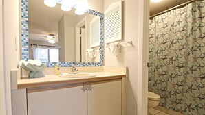 A bathroom with a sink, mirror, and shower curtain. - Ocean Village Club Condo J16 (St. Augustine)