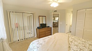 A bedroom with a bed, a dresser, a television on the dresser, a ceiling fan, and a sliding door. - Ocean Village Club Condo J16 (St. Augustine)