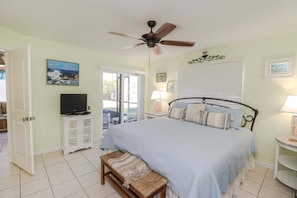 A bedroom with a bed, ceiling fan, television, and a bench.