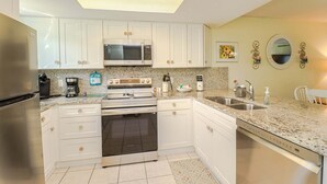 Una cocina con armarios blancos, electrodomésticos de acero inoxidable, microondas, estufa y lavavajillas.