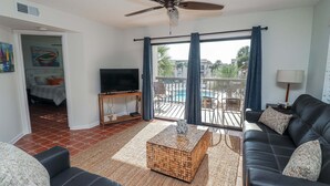 Un soggiorno con divano, tavolino, televisione e un balcone con vista sulla piscina.