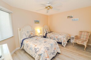 Un dormitorio con dos camas, ventilador de techo, una silla y un calefactor.