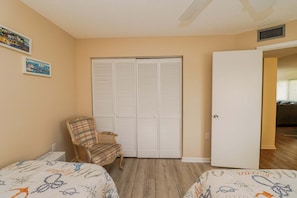 A bedroom with two beds, a chair, a closet, and a door leading to another room.