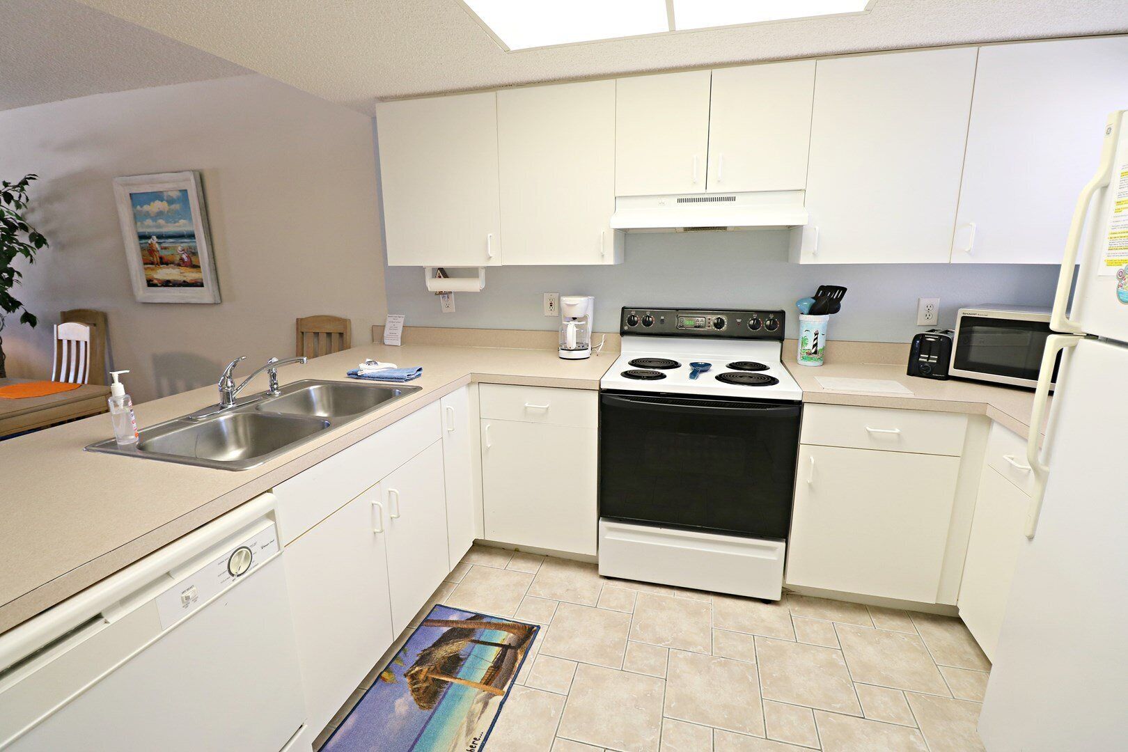 A compact kitchen with white cabinets, a stove, a sink, and a microwave.