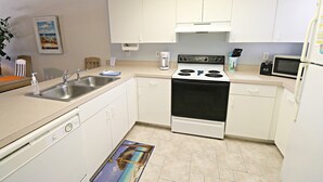 A compact kitchen with white cabinets, a stove, a sink, and a microwave. - Ocean Village Club Condo L24 (St. Augustine)