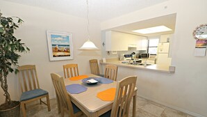 A dining area with a wooden table, chairs, and a potted plant. - Ocean Village Club Condo L24 (St. Augustine)