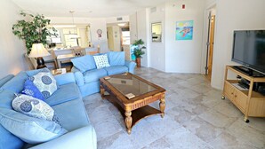 A living room with a blue sofa, a glass coffee table, and a TV on a wooden stand. - Ocean Village Club Condo L24 (St. Augustine)