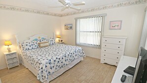 A bedroom with a bed, bedside tables, a dresser, a television, and a window with blinds. - Ocean Village Club Condo L24 (St. Augustine)