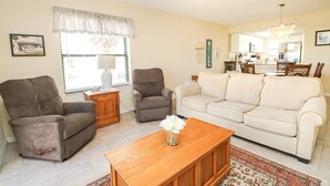 A living room with a beige sofa, two armchairs, a wooden coffee table, and a window with curtains. - Ocean Village Club Condo L26 (St. Augustine)