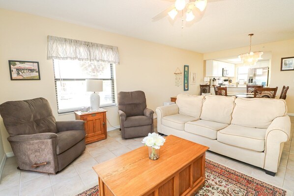 A living room with a beige sofa, two armchairs, a wooden coffee table, and a window with curtains.