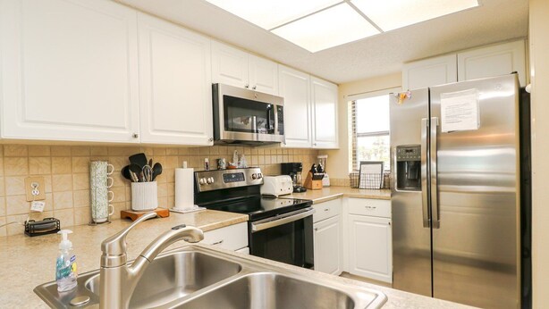 A modern kitchen with white cabinets, stainless steel appliances, a double sink, and a microwave above the stove. - Ocean Village Club Condo L26 (St. Augustine)