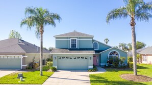 A two-story house with a garage, a front yard with palm trees, and a clear blue sky. - Luxurious Lake House, minutes from Disney (Kissimmee)