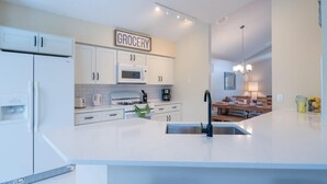 A modern kitchen with white cabinetry, a built-in microwave, a gas stove, and a sink with a faucet. A 'GROCERY' sign is visible above the cabinets. - Luxurious Lake House, minutes from Disney (Kissimmee)