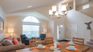 A dining area with a wooden table set for four, surrounded by two armchairs and a sofa. - Luxurious Lake House, minutes from Disney (Kissimmee)