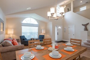 Un coin repas avec une table en bois dressée pour quatre personnes, entourée de deux fauteuils et d’un canapé.
