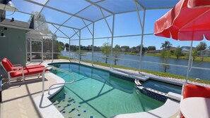 A pool area with a glass enclosure, red lounge chairs, and a view of a lake.