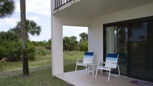 Un espace extérieur abrité comprenant deux chaises blanches et une porte vitrée donnant accès à une piscine.