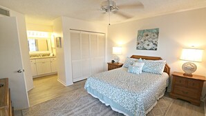 Een slaapkamer met een bed, nachtkastjes, een hanglamp, een schilderij en een inloopkast.