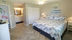 A bedroom with a bed, a nightstand, a ceiling fan, a closet, and a bathroom with a mirror and sink. - Ocean Village Club Condo O32 (St. Augustine)