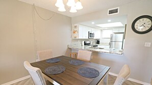 A dining area with a wooden table, four chairs, and a chandelier. - Ocean Village Club Condo O32 (St. Augustine)