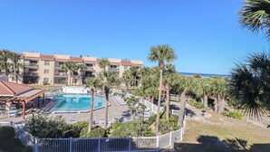 Un hôtel doté d’une piscine entourée de palmiers, offrant une vue sur la plage et comprenant plusieurs balcons.