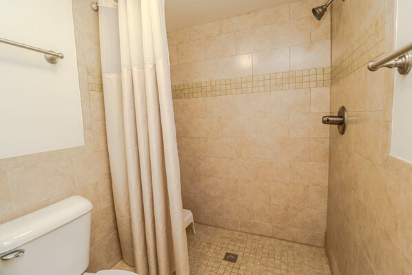A bathroom with a shower, toilet, and a tiled floor.