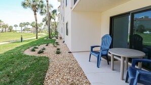 Een balkon met een tafel en twee stoelen, een grindpad en palmstruiken.