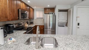 A modern kitchen with wooden cabinets, stainless steel appliances, a granite countertop, and a double sink. - Ocean Village Club Condo P18 (St. Augustine)