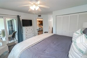Une chambre à coucher comprenant un lit, une télévision, une armoire et un ventilateur de plafond.