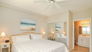 Ein Schlafzimmer mit Bett, Nachttischen, Deckenventilator, großem Spiegel und einem Badezimmer mit Waschbecken und Waschtisch.