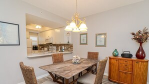 A dining area with a wooden table, wicker chairs, a wooden cabinet, and a mirror above the counter.