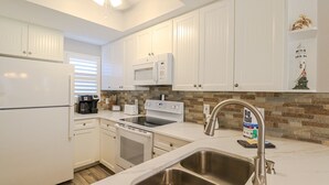 A modern kitchen with white cabinets, a stainless steel sink, a microwave, a stove, and a coffee maker.