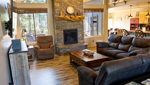 A spacious living room with a stone fireplace, leather sofas, and a wooden coffee table. - Modern Cabin Escape with Incredible Pine Tree Views! (Lakeside)