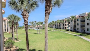 A hotel courtyard with palm trees, a swimming pool, and a building with balconies.