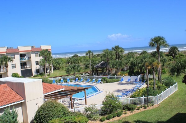 A hotel with a pool, beach chairs, and a view of the ocean.