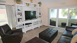 Ein Wohnzimmer mit Fernseher, weißer Unterhaltungseinheit, braunen Ledersofas und einer Schiebetür zum Außenbereich.