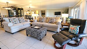 Ein geräumiges Wohnzimmer mit zwei Sofas, einem osmanischen Hocker mit ZEBRA-Muster, einem schwarzen Ledersessel und einem Essbereich im Hintergrund.