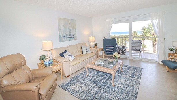 Ein Wohnzimmer mit Sofa, Sesseln, Couchtisch und Meerblick durch große Fenster.