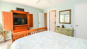 Une chambre à coucher comprenant un lit, une armoire en bois avec un téléviseur, une commode, un miroir et un ventilateur de plafond.