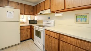 Cocina compacta con armarios de madera, refrigerador, microondas y estufa.