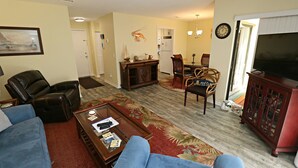 A living room with a sofa, a coffee table, a dining table with chairs, a television, and a decorative lobster on the wall.
